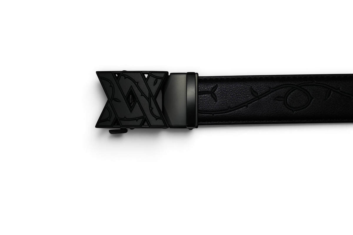 VASANA automatic belt buckle in matte black with an engraved V monogram and vine detailing on a black leather strap